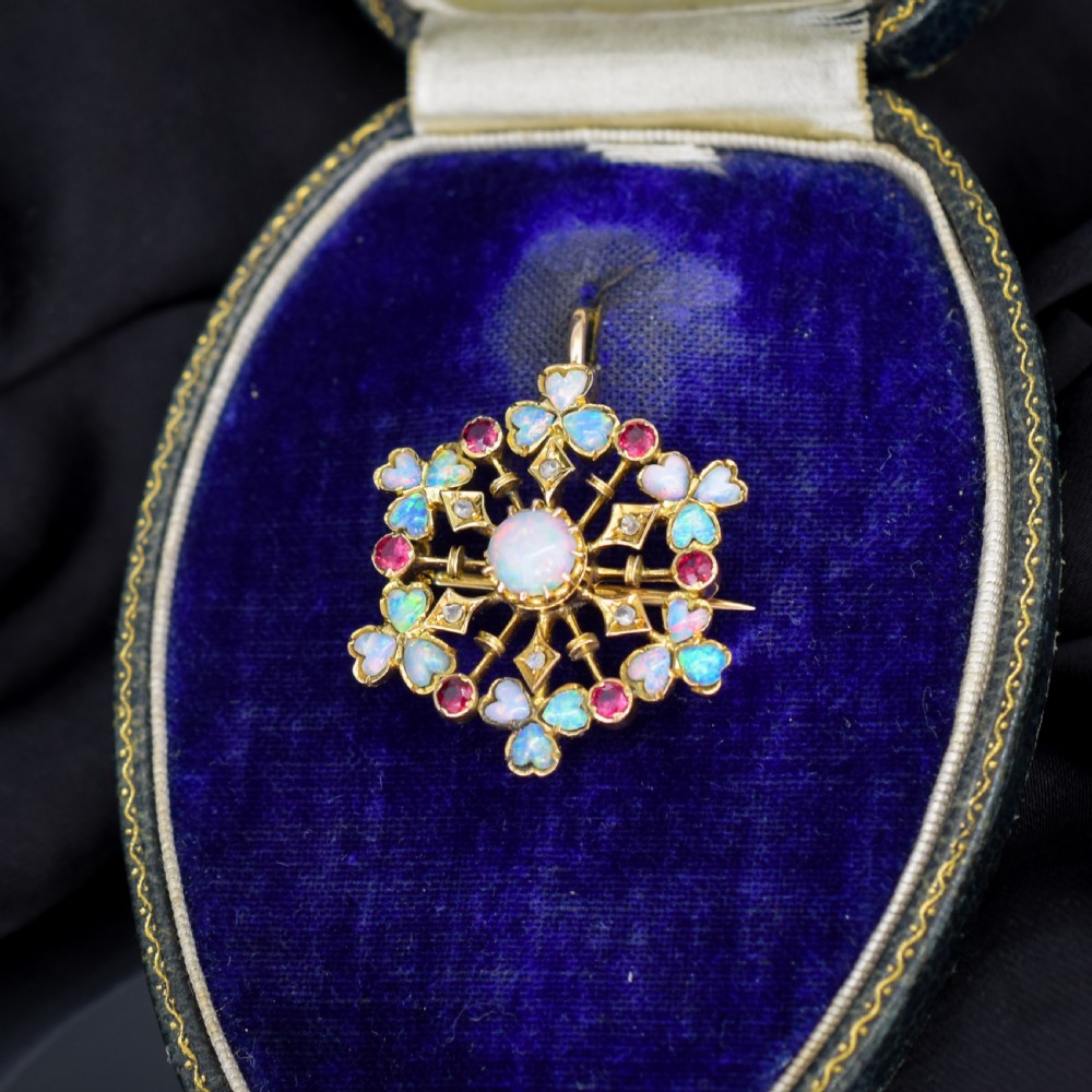 A gold starburst-shaped brooch and pendant set with a central cabochon opal surrounded by rubies, diamonds, and heart-shaped opal petals. View II