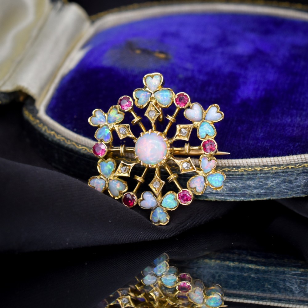A gold starburst-shaped brooch and pendant set with a central cabochon opal surrounded by rubies, diamonds, and heart-shaped opal petals. View IV