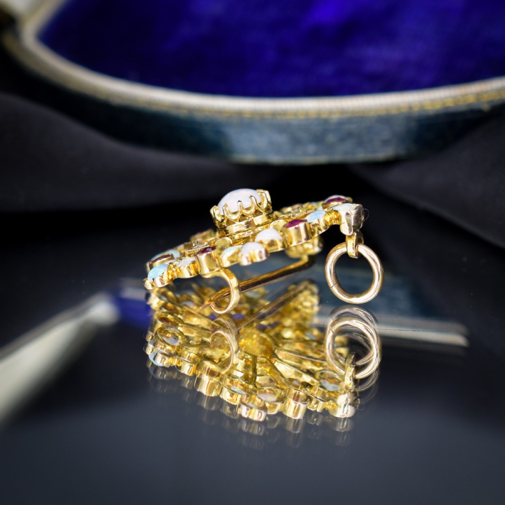 A gold starburst-shaped brooch and pendant set with a central cabochon opal surrounded by rubies, diamonds, and heart-shaped opal petals. View V