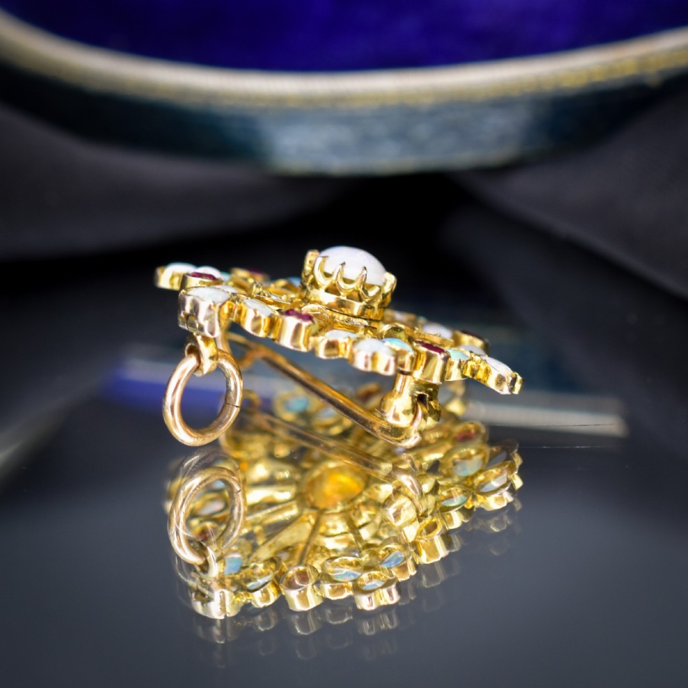 A gold starburst-shaped brooch and pendant set with a central cabochon opal surrounded by rubies, diamonds, and heart-shaped opal petals. View VI