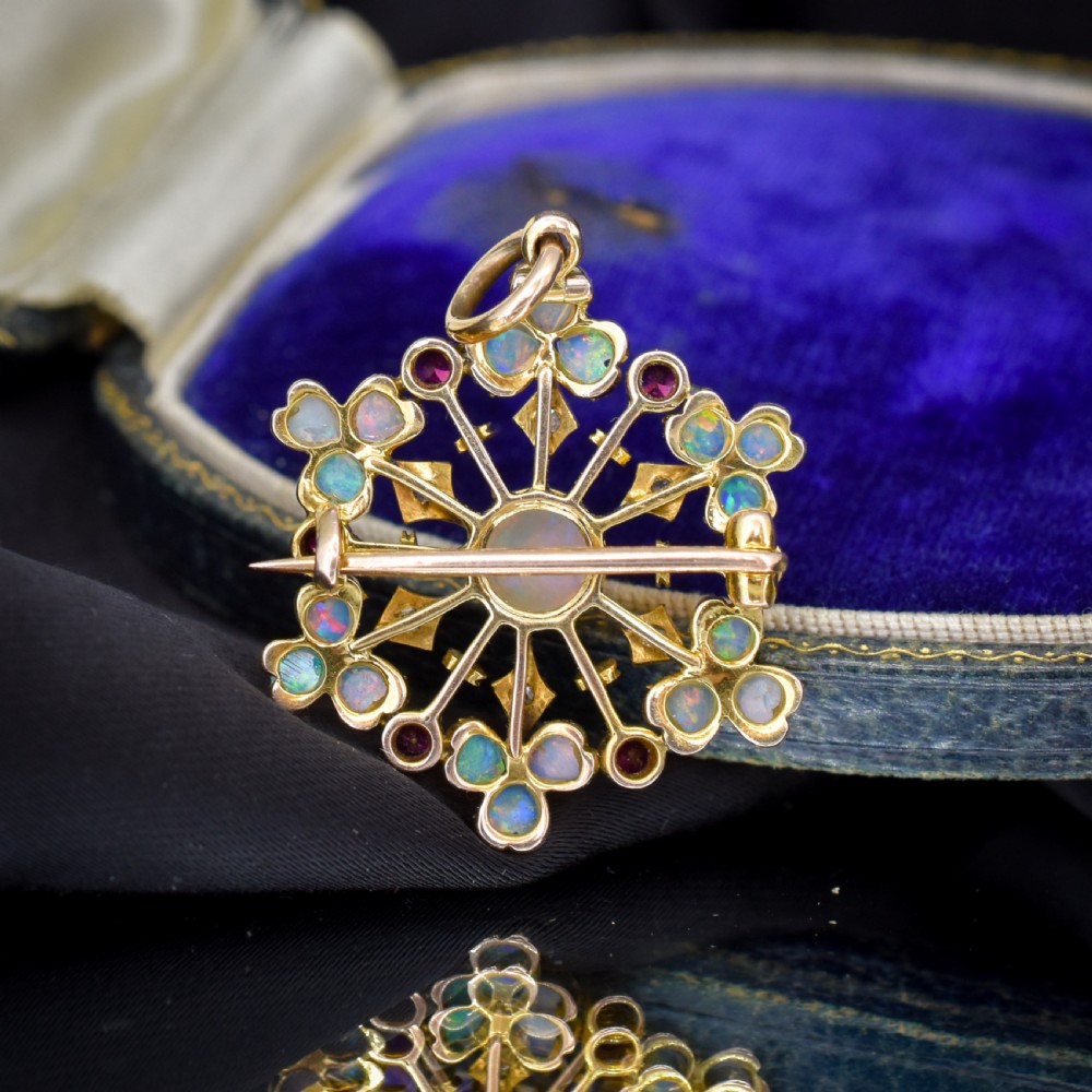 A gold starburst-shaped brooch and pendant set with a central cabochon opal surrounded by rubies, diamonds, and heart-shaped opal petals. View VII