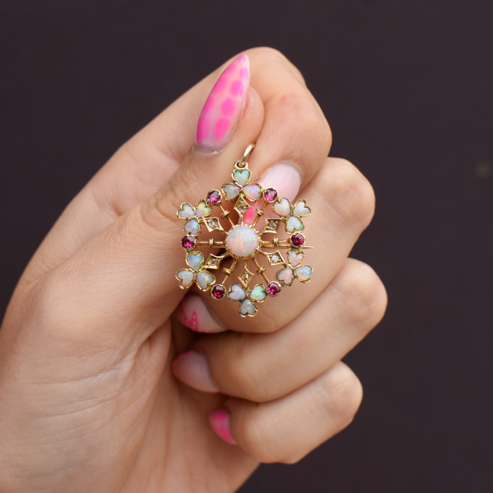 A gold starburst-shaped brooch and pendant set with a central cabochon opal surrounded by rubies, diamonds, and heart-shaped opal petals. View VIII