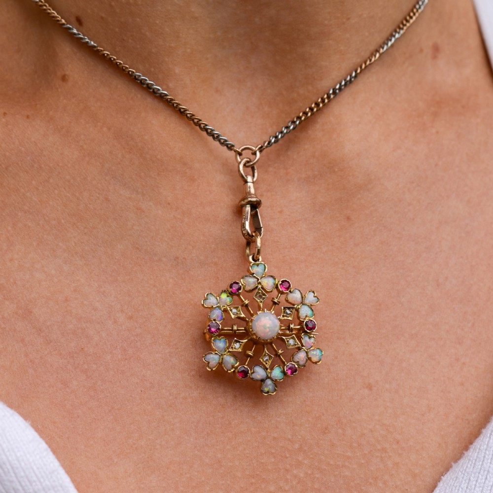 A gold starburst-shaped brooch and pendant set with a central cabochon opal surrounded by rubies, diamonds, and heart-shaped opal petals. View IX