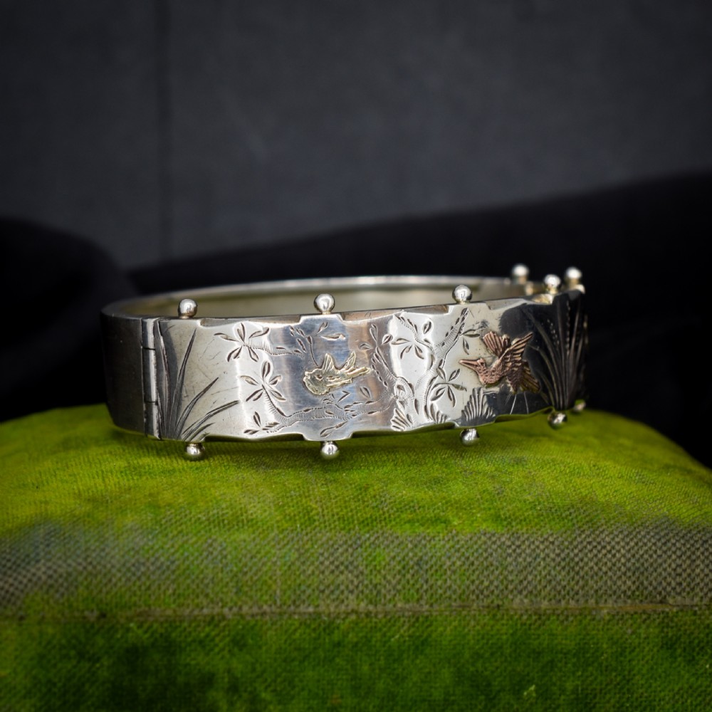 A wide silver hinged cuff bangle featuring engraved floral foliage and applied gold bird motifs along the outer band.