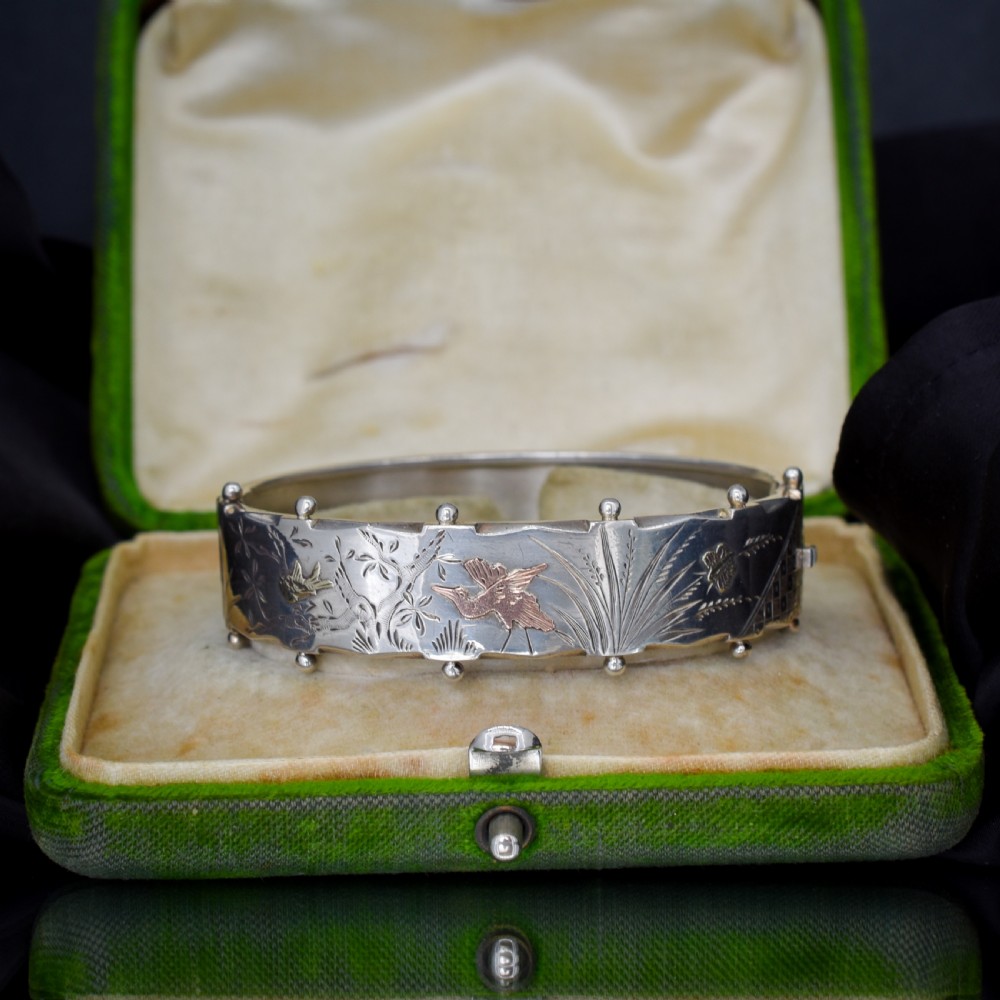 A wide silver hinged cuff bangle featuring engraved floral foliage and applied gold bird motifs along the outer band. View V