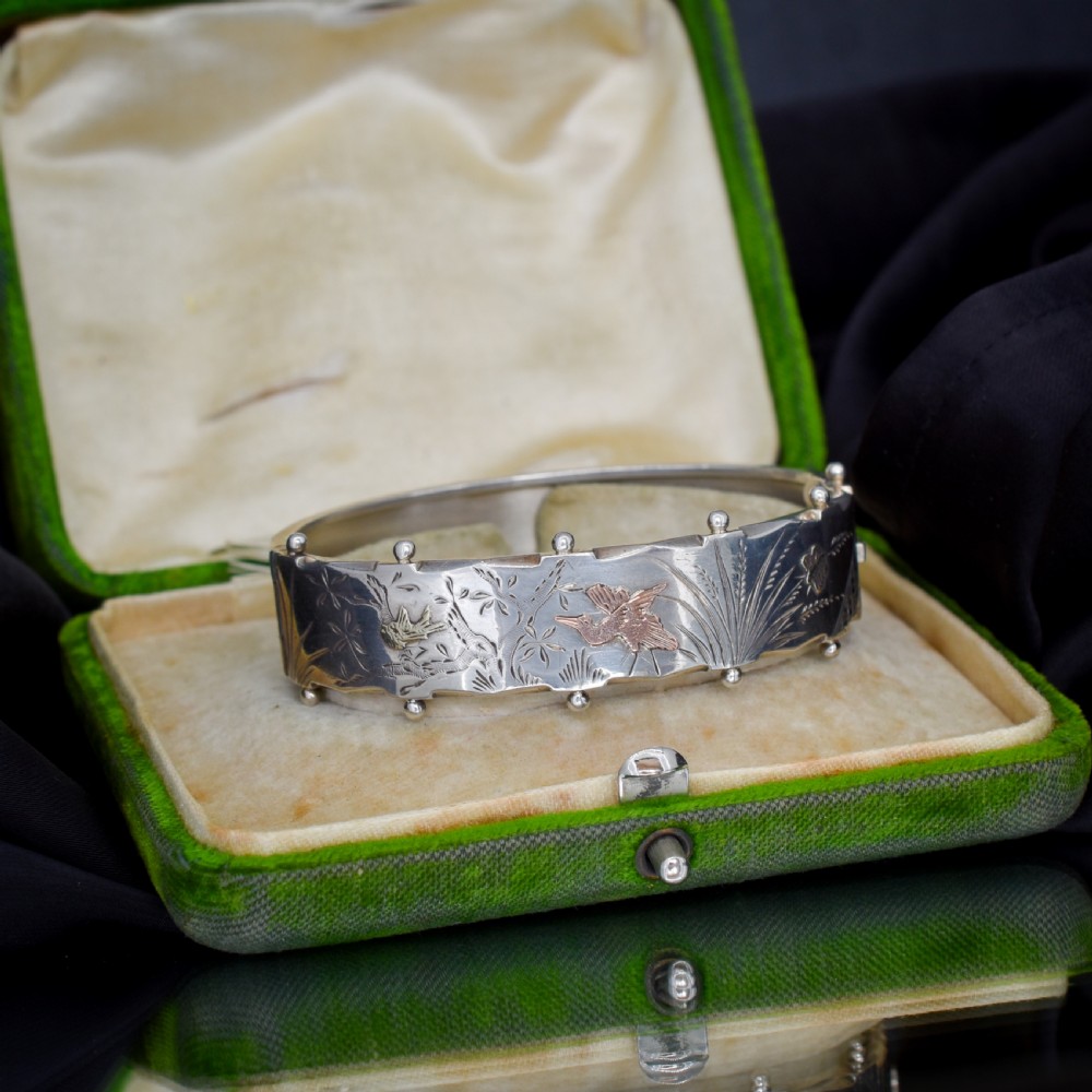 A wide silver hinged cuff bangle featuring engraved floral foliage and applied gold bird motifs along the outer band. View VI