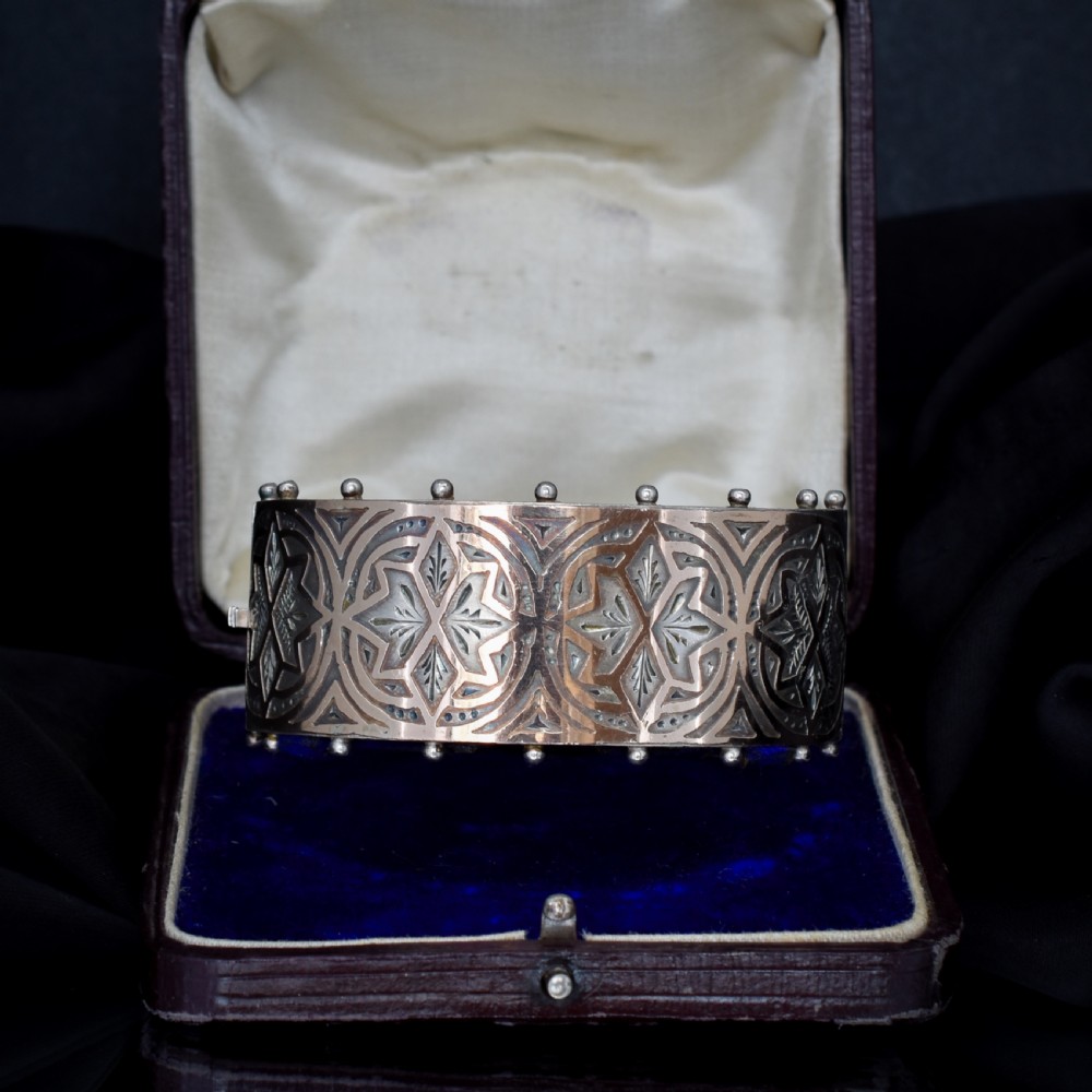 An antique Victorian wide hinged silver bangle decorated with hand-engraved geometric star motifs and a beaded upper and lower rim.