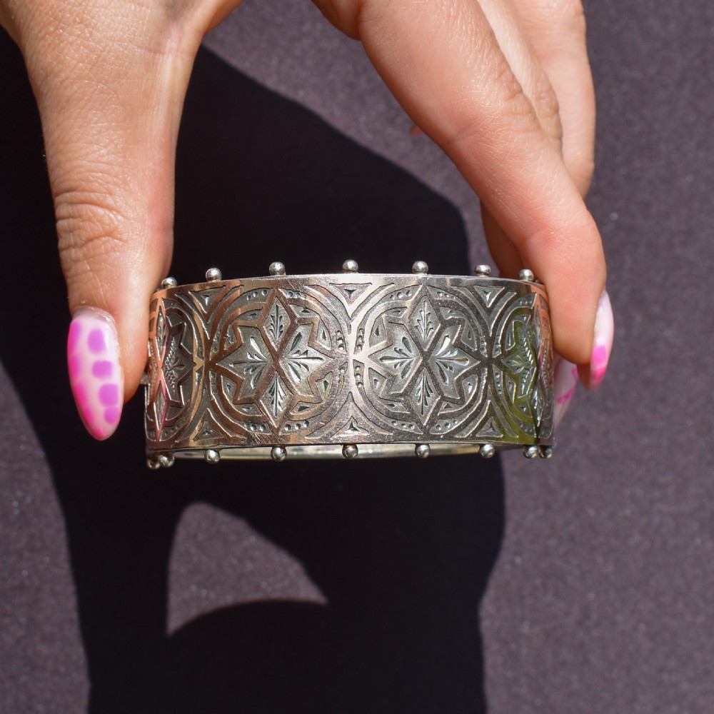 An antique Victorian wide hinged silver bangle decorated with hand-engraved geometric star motifs and a beaded upper and lower rim. View X