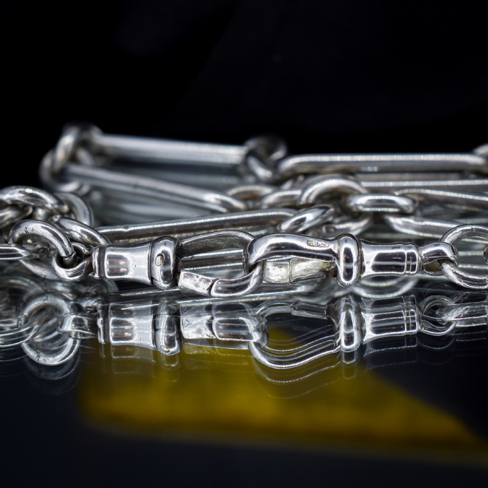 An antique Edwardian sterling silver trombone link Albert watch chain featuring a T-bar and swivel clasp displayed on a velvet background. View V