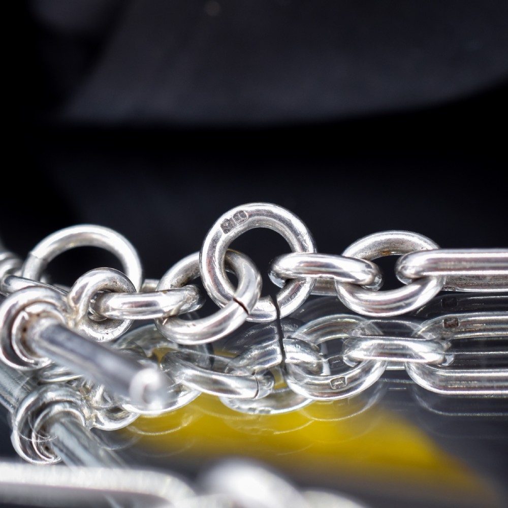 An antique Edwardian sterling silver trombone link Albert watch chain featuring a T-bar and swivel clasp displayed on a velvet background. View VI