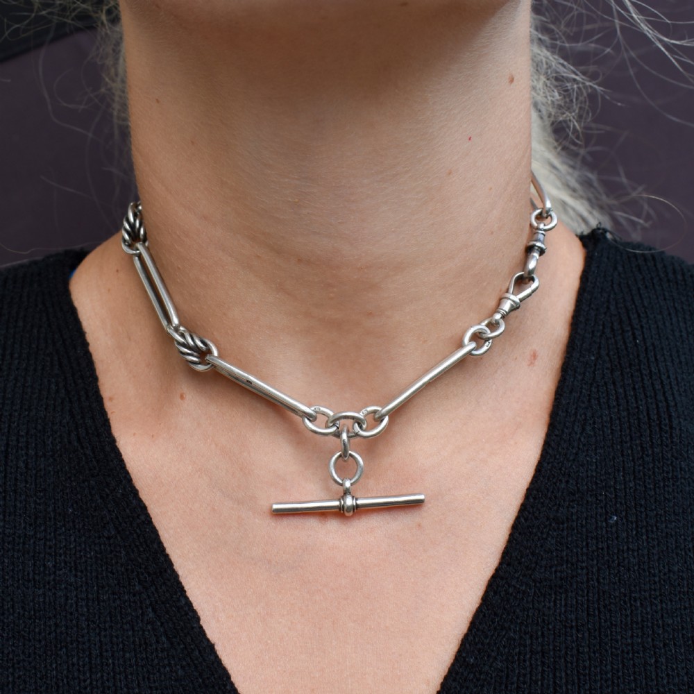 An antique Edwardian sterling silver trombone link Albert watch chain featuring a T-bar and swivel clasp displayed on a velvet background. View VIII