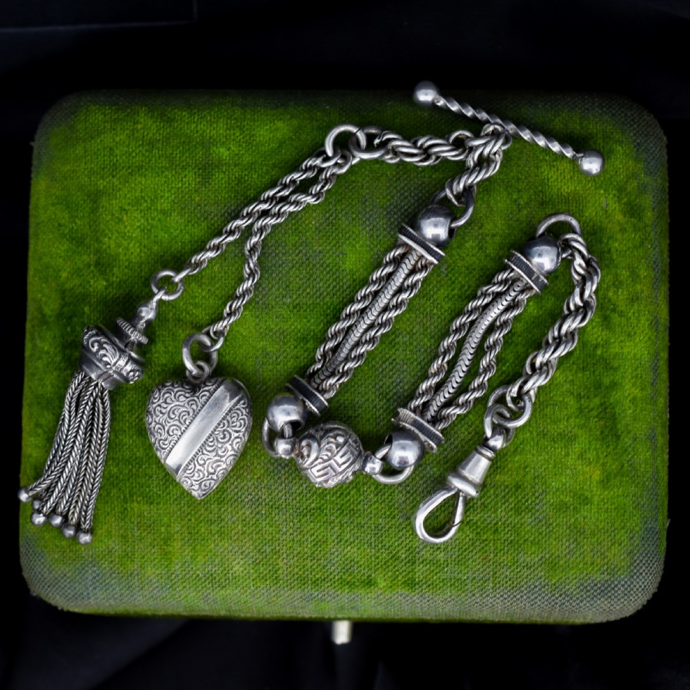An antique silver Albertina watch chain styled as a bracelet, featuring multi-strand rope chains, an engraved heart motif charm, a silver tassel, a T-bar, and a swivel clasp.