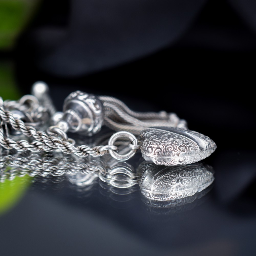 An antique silver Albertina watch chain styled as a bracelet, featuring multi-strand rope chains, an engraved heart motif charm, a silver tassel, a T-bar, and a swivel clasp. View V