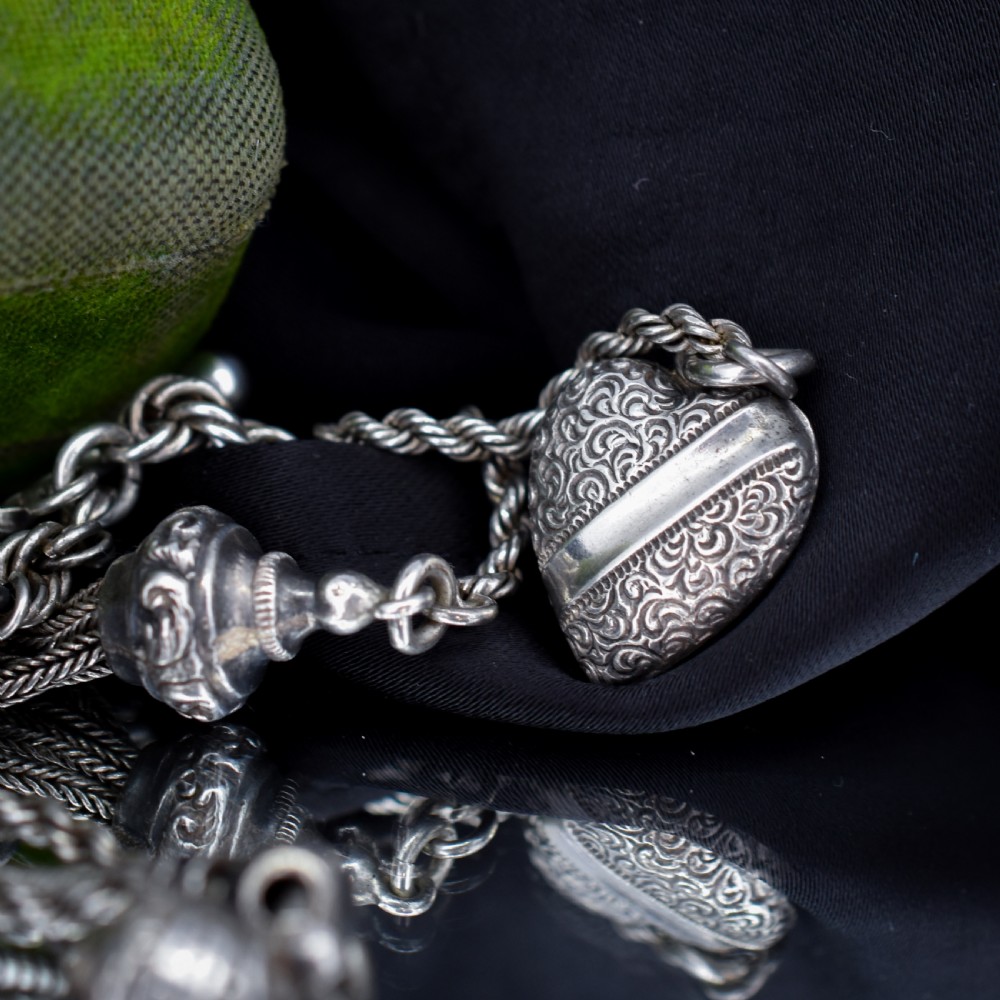 An antique silver Albertina watch chain styled as a bracelet, featuring multi-strand rope chains, an engraved heart motif charm, a silver tassel, a T-bar, and a swivel clasp. View VI
