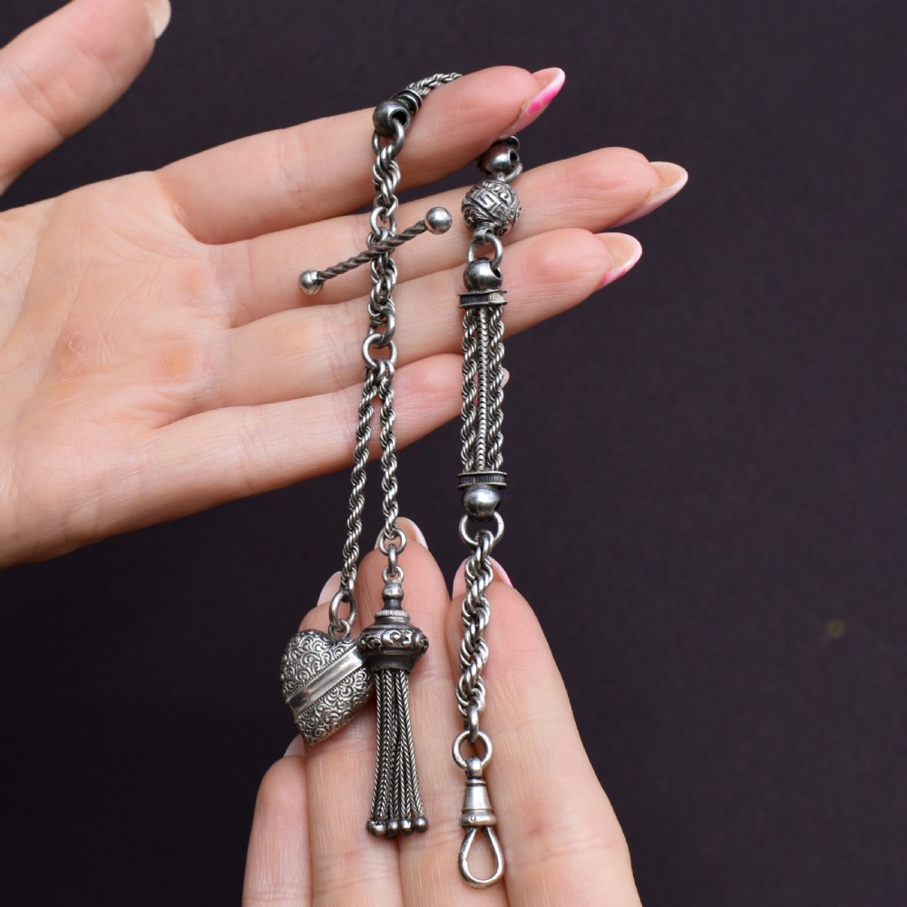 An antique silver Albertina watch chain styled as a bracelet, featuring multi-strand rope chains, an engraved heart motif charm, a silver tassel, a T-bar, and a swivel clasp. View VIII