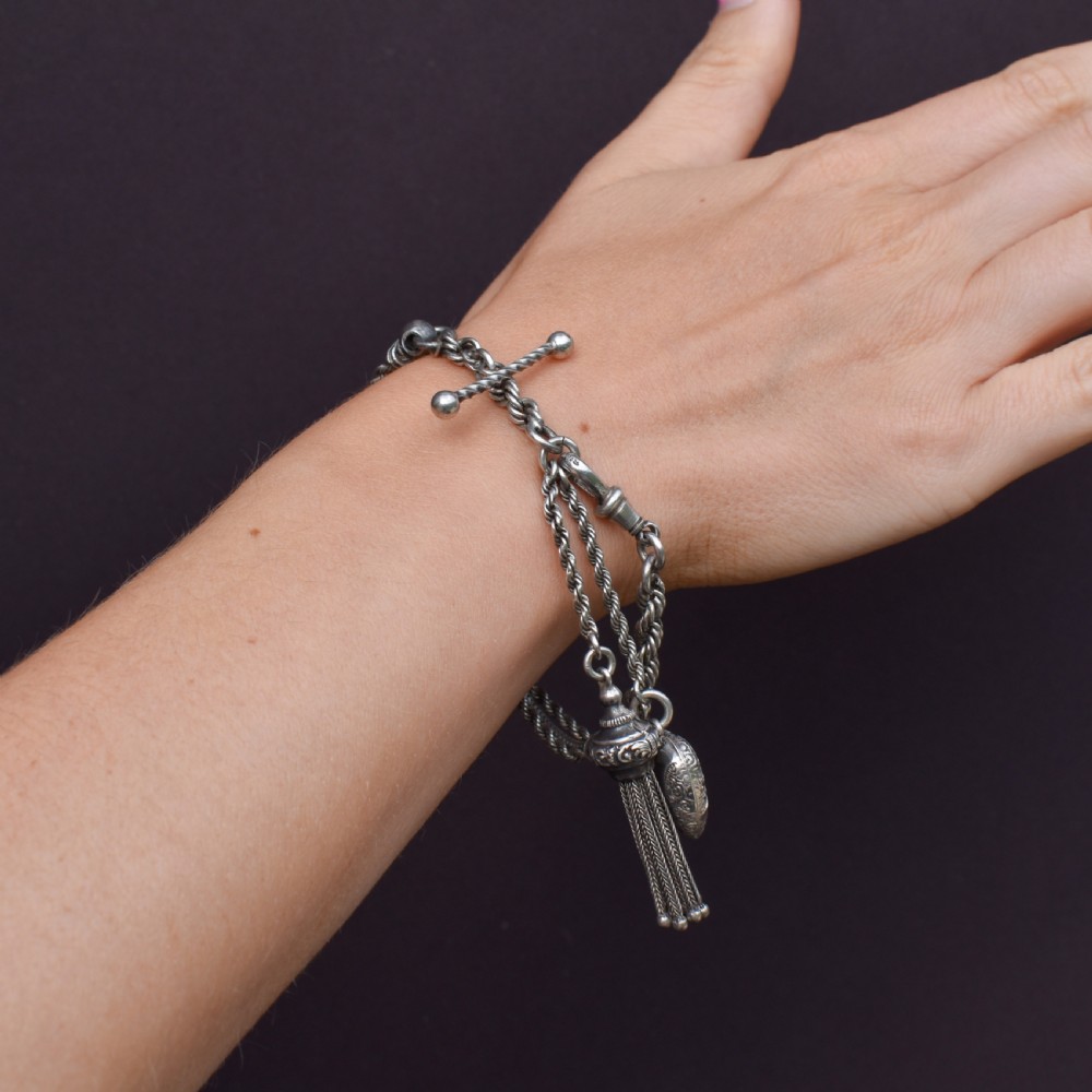 An antique silver Albertina watch chain styled as a bracelet, featuring multi-strand rope chains, an engraved heart motif charm, a silver tassel, a T-bar, and a swivel clasp. View IX