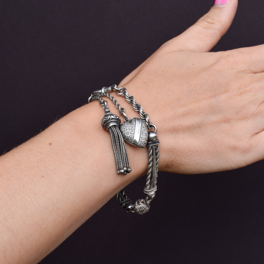 An antique silver Albertina watch chain styled as a bracelet, featuring multi-strand rope chains, an engraved heart motif charm, a silver tassel, a T-bar, and a swivel clasp. View X