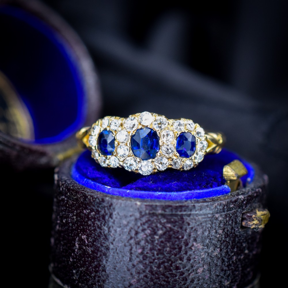 An 18ct yellow gold Victorian ring featuring three oval blue sapphires, each encircled by a cluster of small diamonds.