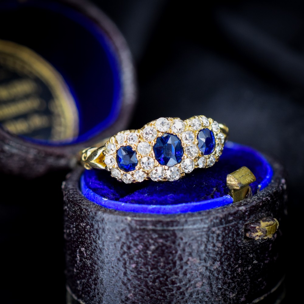 An 18ct yellow gold Victorian ring featuring three oval blue sapphires, each encircled by a cluster of small diamonds. View II