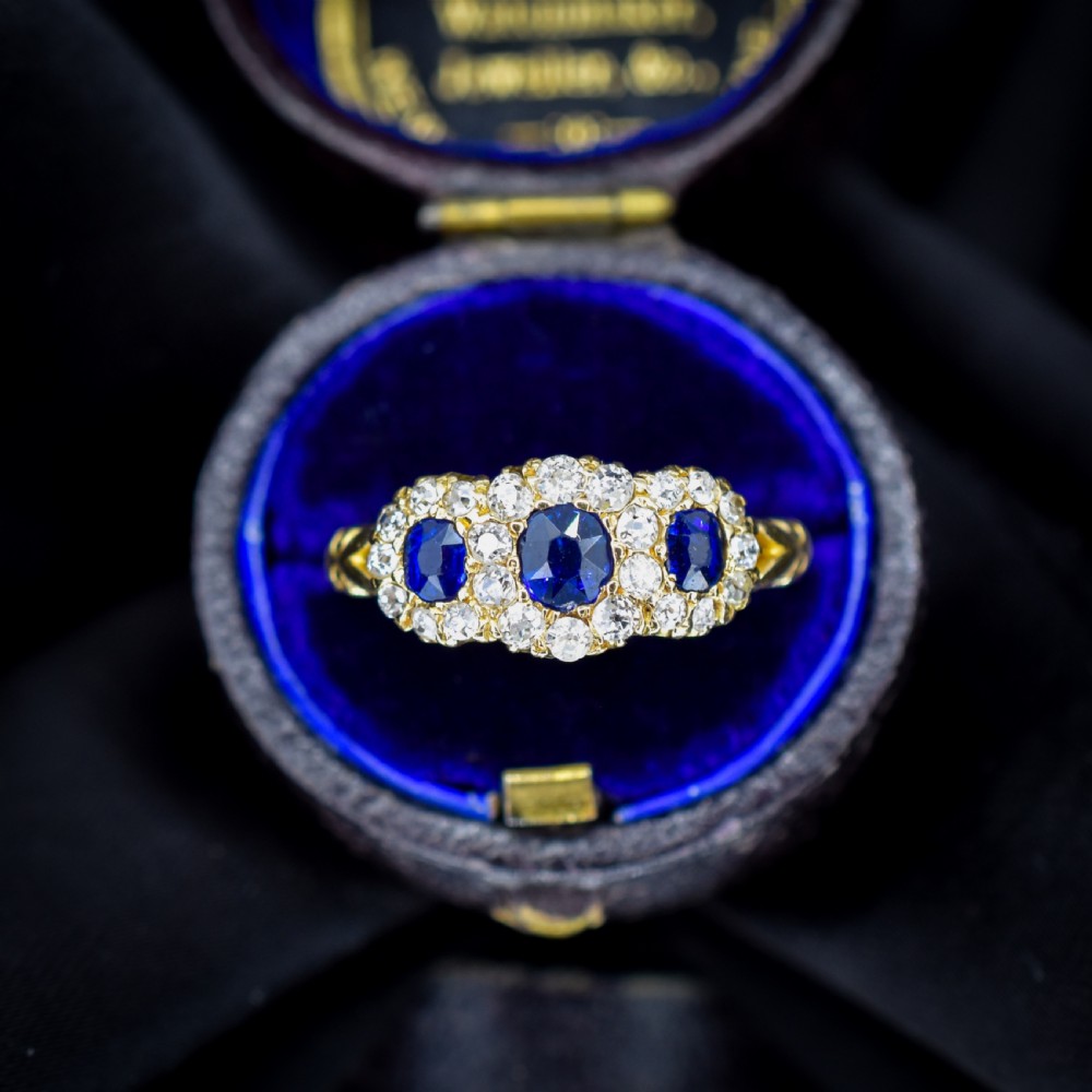 An 18ct yellow gold Victorian ring featuring three oval blue sapphires, each encircled by a cluster of small diamonds. View III