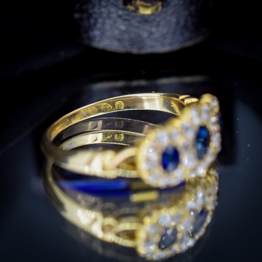 An 18ct yellow gold Victorian ring featuring three oval blue sapphires, each encircled by a cluster of small diamonds. View VII