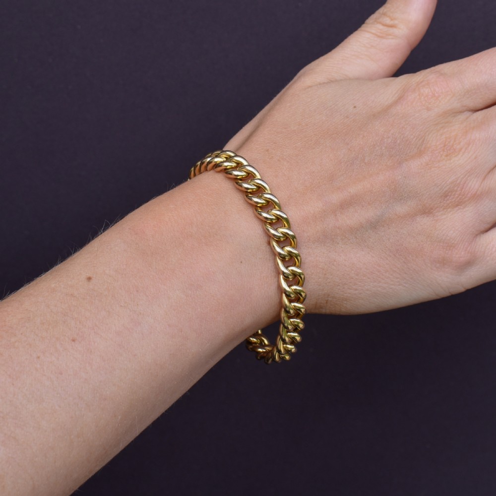 An 18ct yellow gold curb link bracelet featuring a concealed box clasp and an attached safety chain. View IX