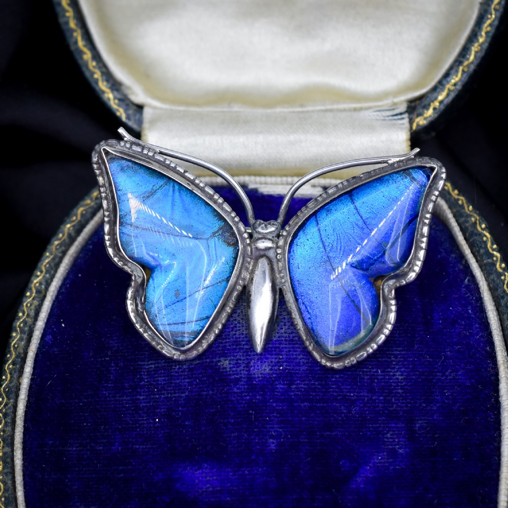 An Art Deco sterling silver butterfly brooch featuring vibrant iridescent blue butterfly wing panels beneath glass.