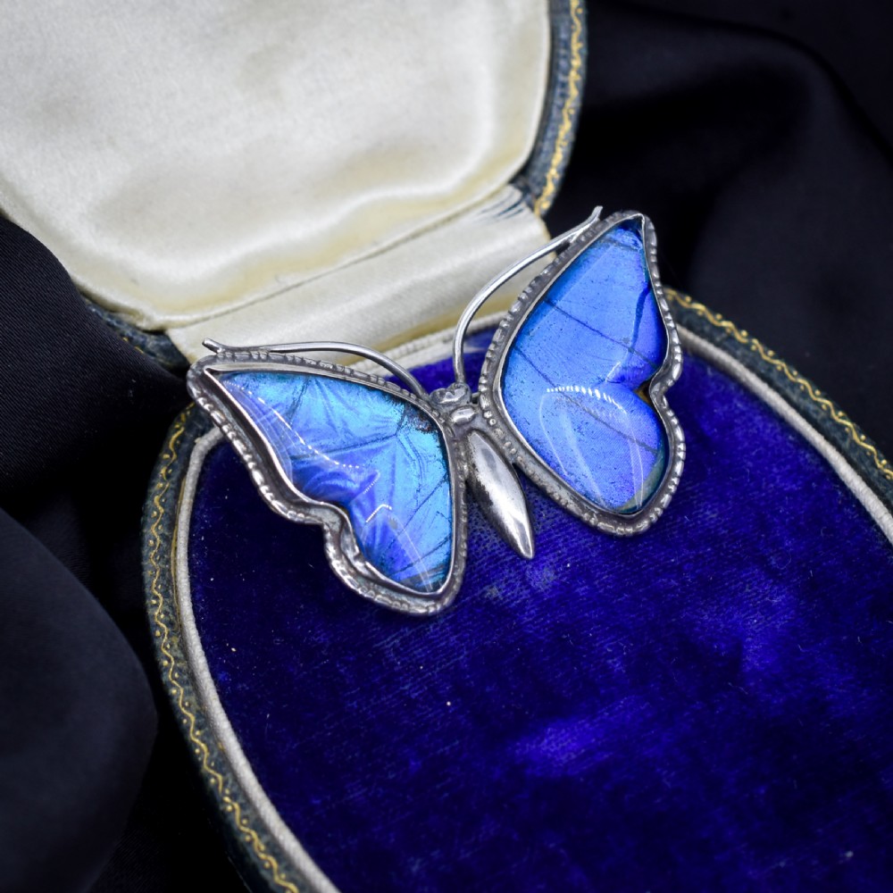 An Art Deco sterling silver butterfly brooch featuring vibrant iridescent blue butterfly wing panels beneath glass. View III