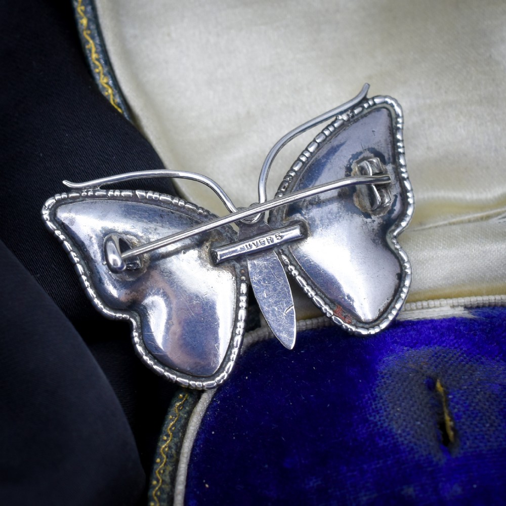 An Art Deco sterling silver butterfly brooch featuring vibrant iridescent blue butterfly wing panels beneath glass. View IV