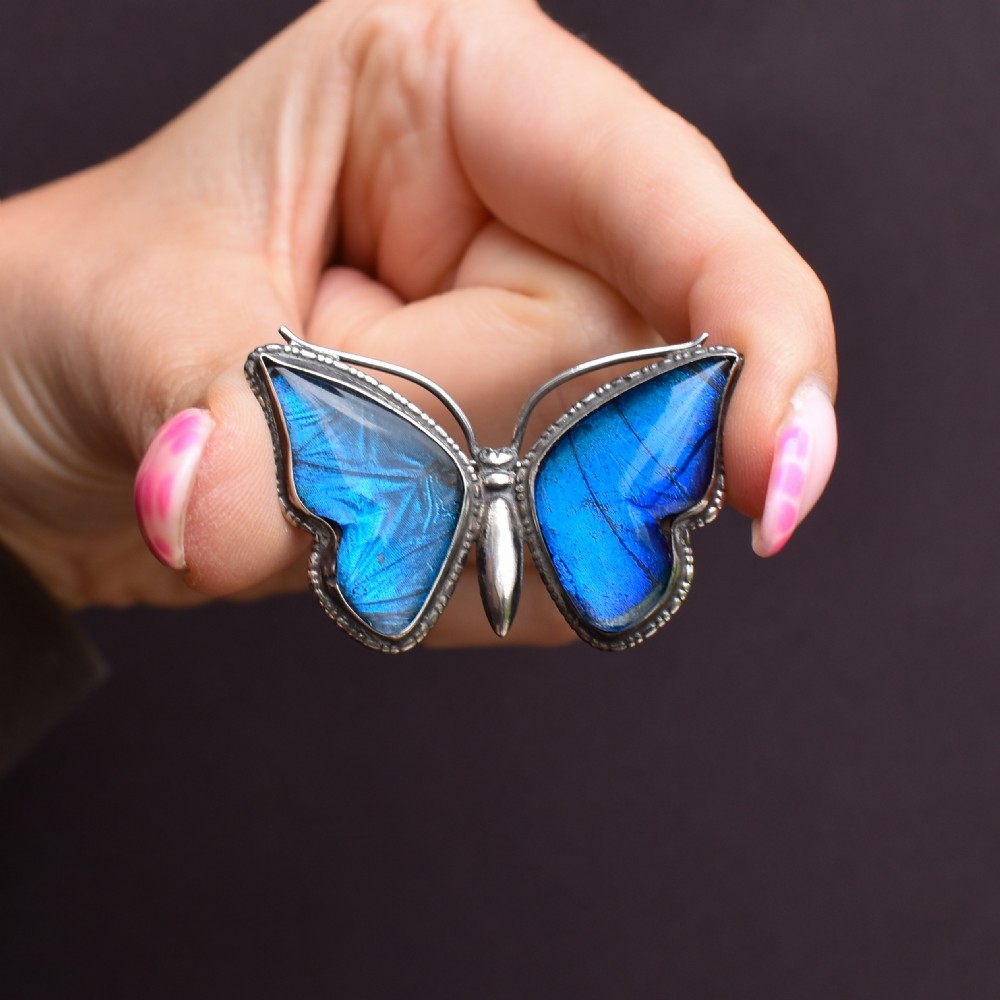 An Art Deco sterling silver butterfly brooch featuring vibrant iridescent blue butterfly wing panels beneath glass. View VIII