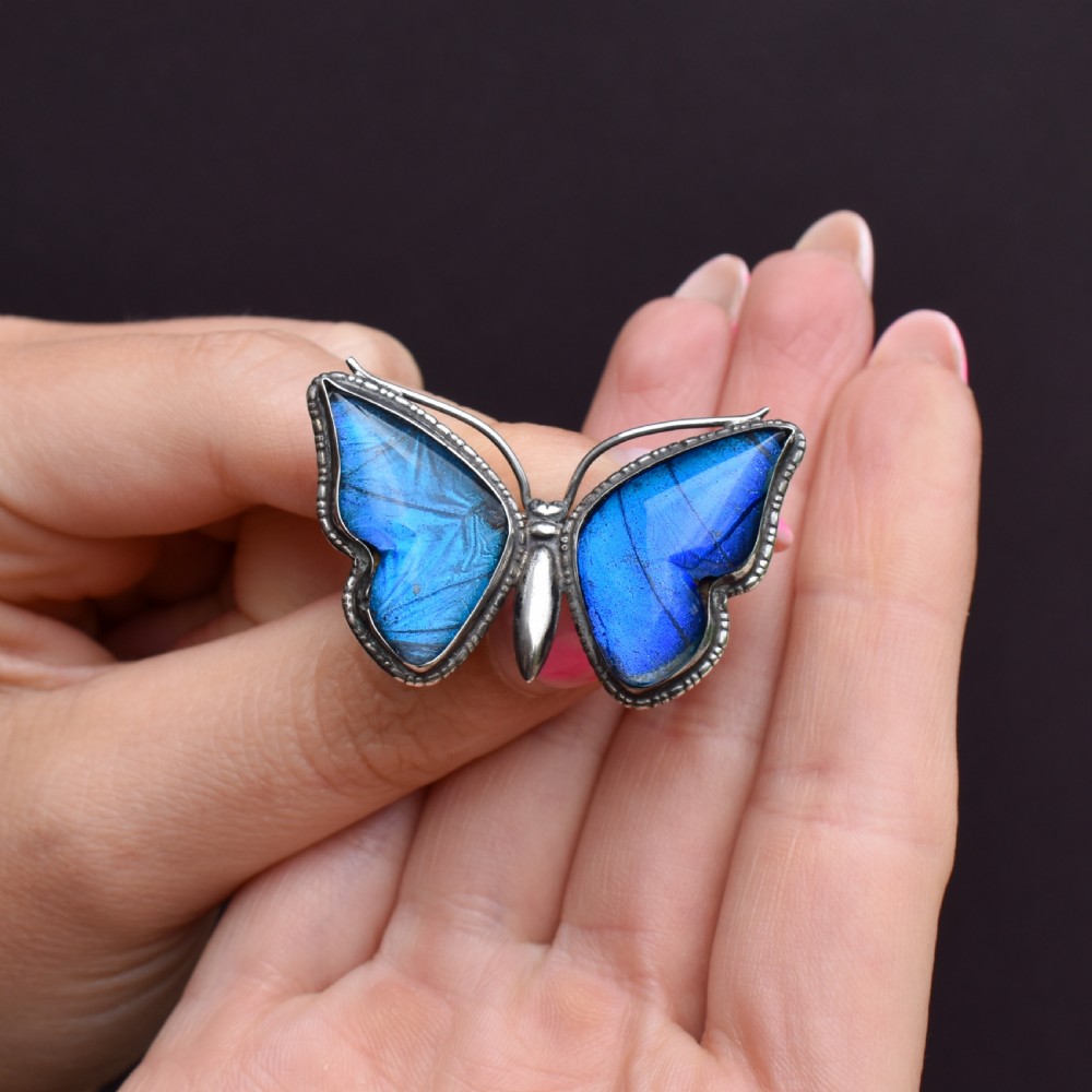 An Art Deco sterling silver butterfly brooch featuring vibrant iridescent blue butterfly wing panels beneath glass. View IX