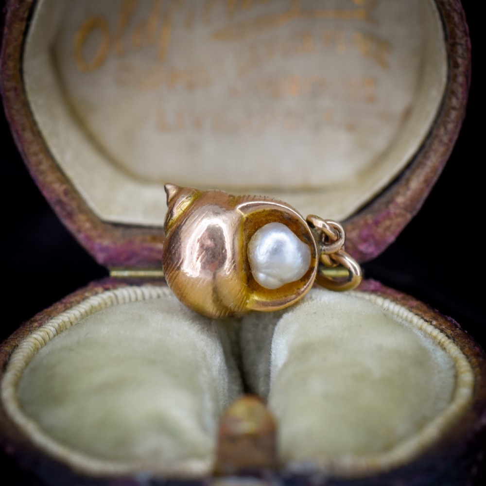 A 9ct yellow gold seashell charm enclosing a single pearl with a top suspension loop.