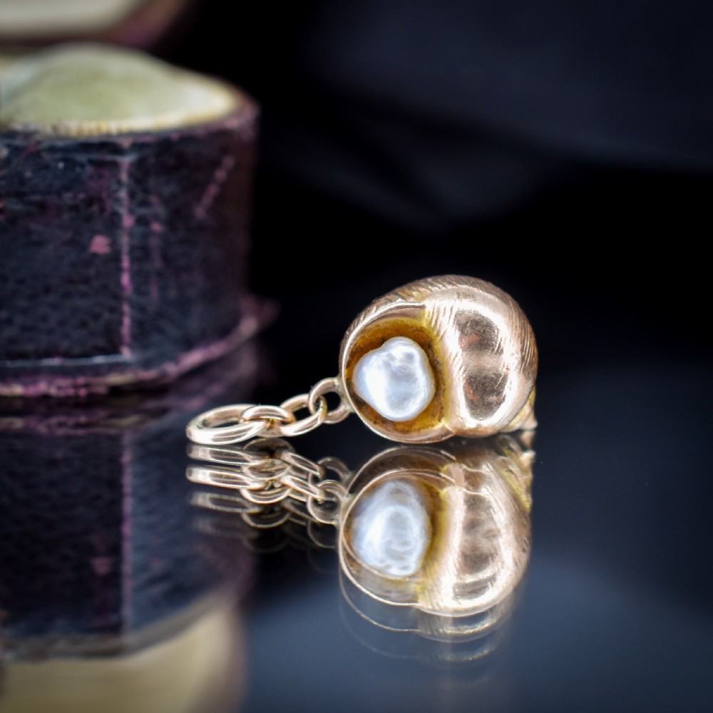 A 9ct yellow gold seashell charm enclosing a single pearl with a top suspension loop. View V