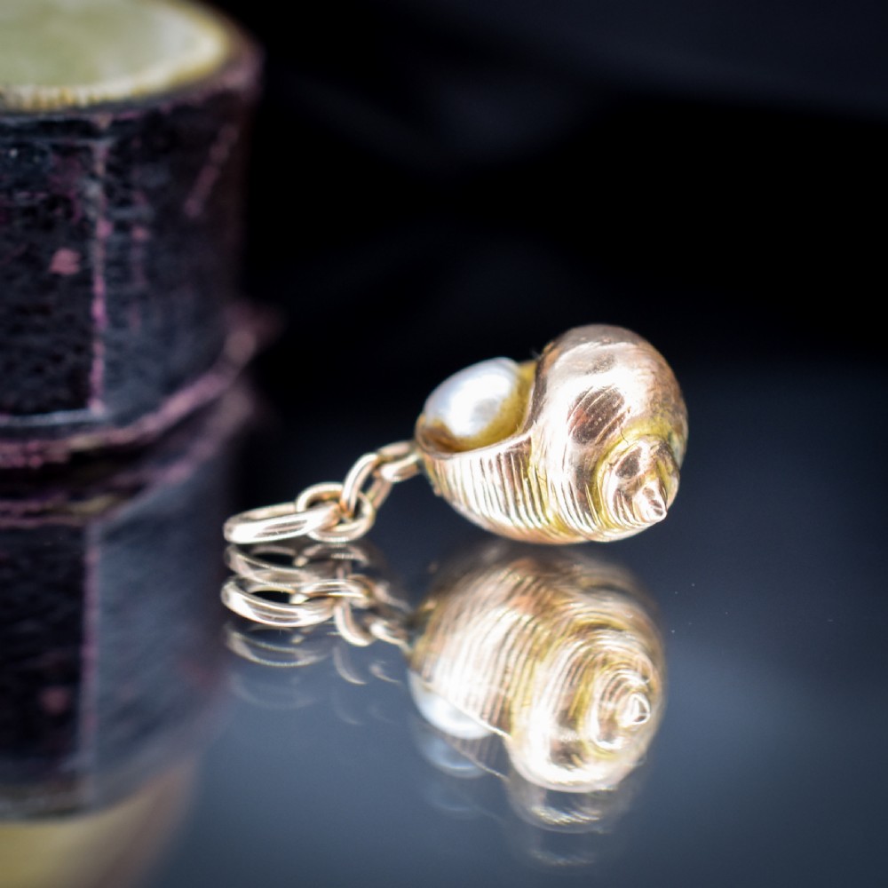 A 9ct yellow gold seashell charm enclosing a single pearl with a top suspension loop. View VI