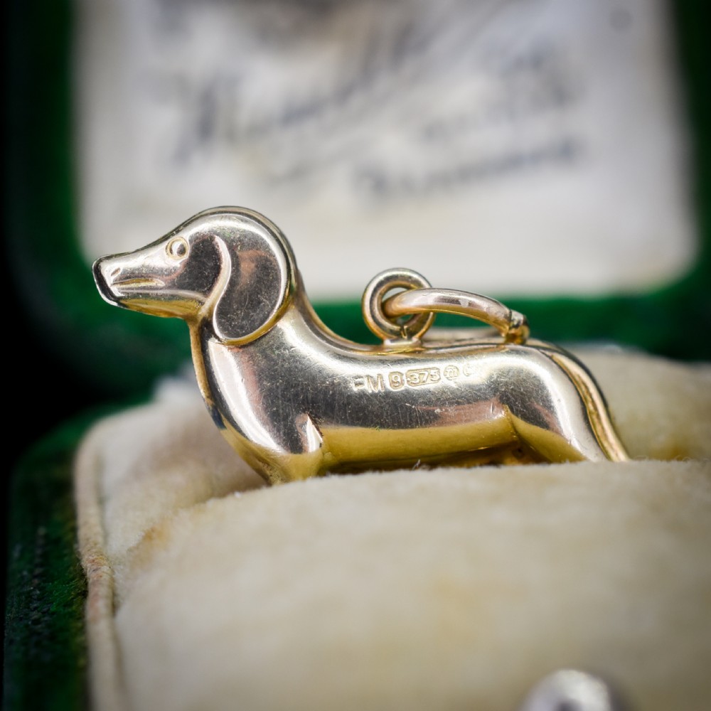 A solid 9ct yellow gold dachshund dog charm featuring detailed eye engravings and visible hallmarks along its body.