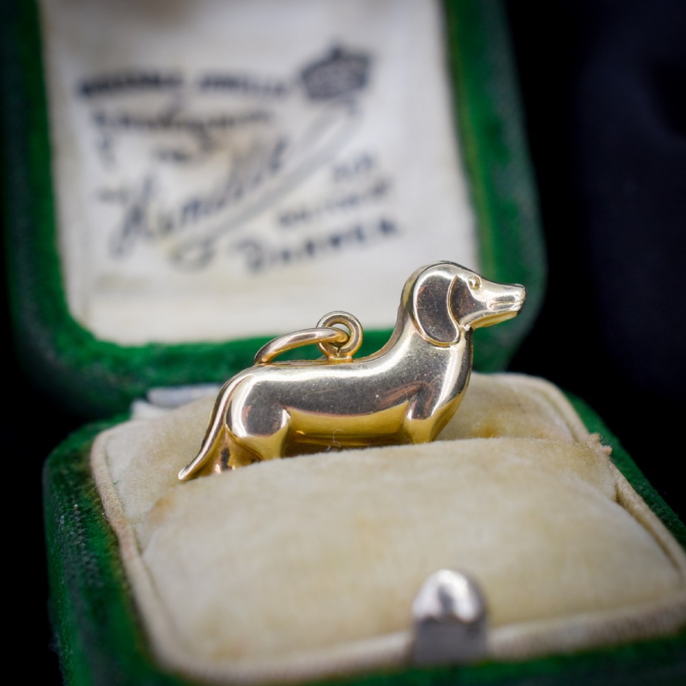 A solid 9ct yellow gold dachshund dog charm featuring detailed eye engravings and visible hallmarks along its body. View II