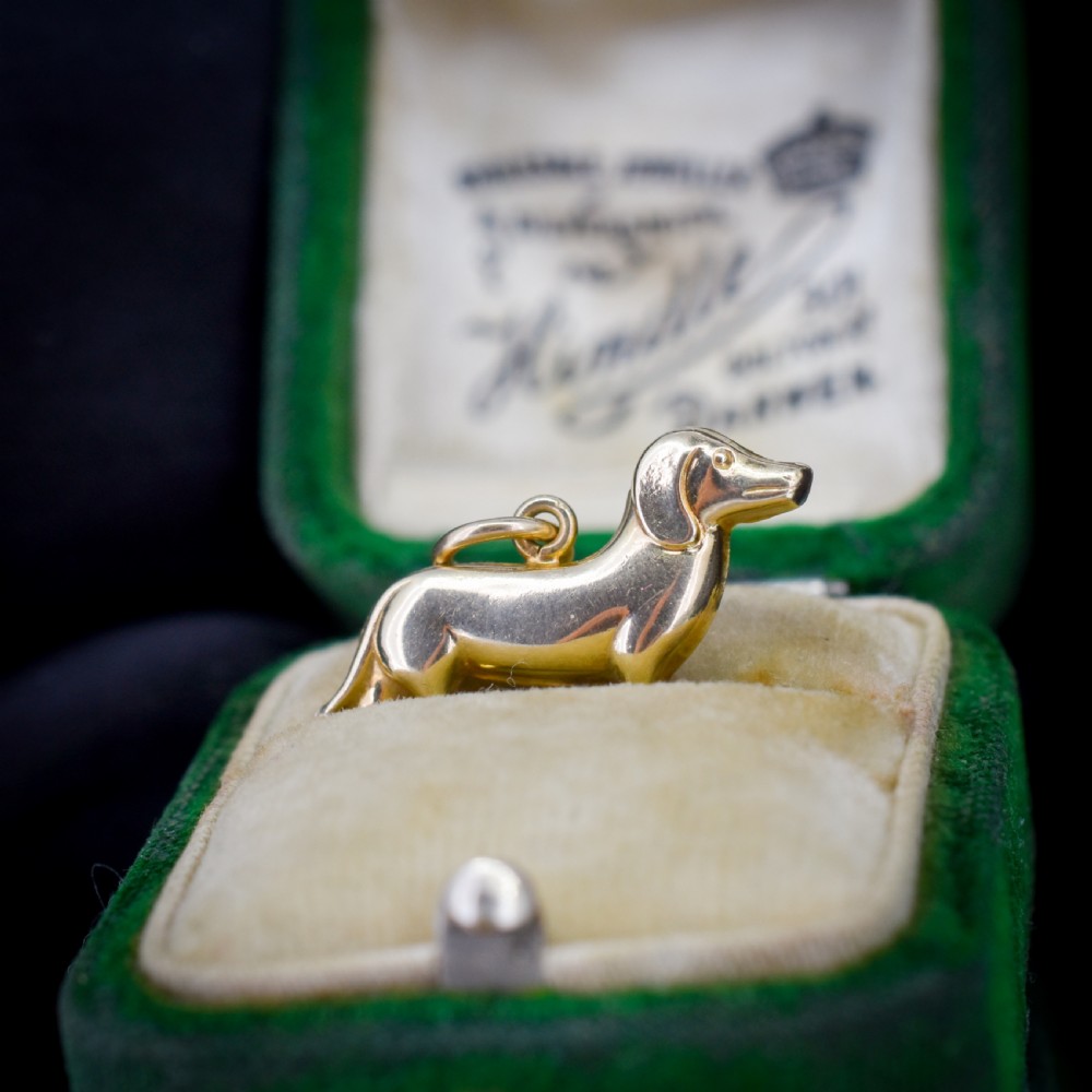 A solid 9ct yellow gold dachshund dog charm featuring detailed eye engravings and visible hallmarks along its body. View III