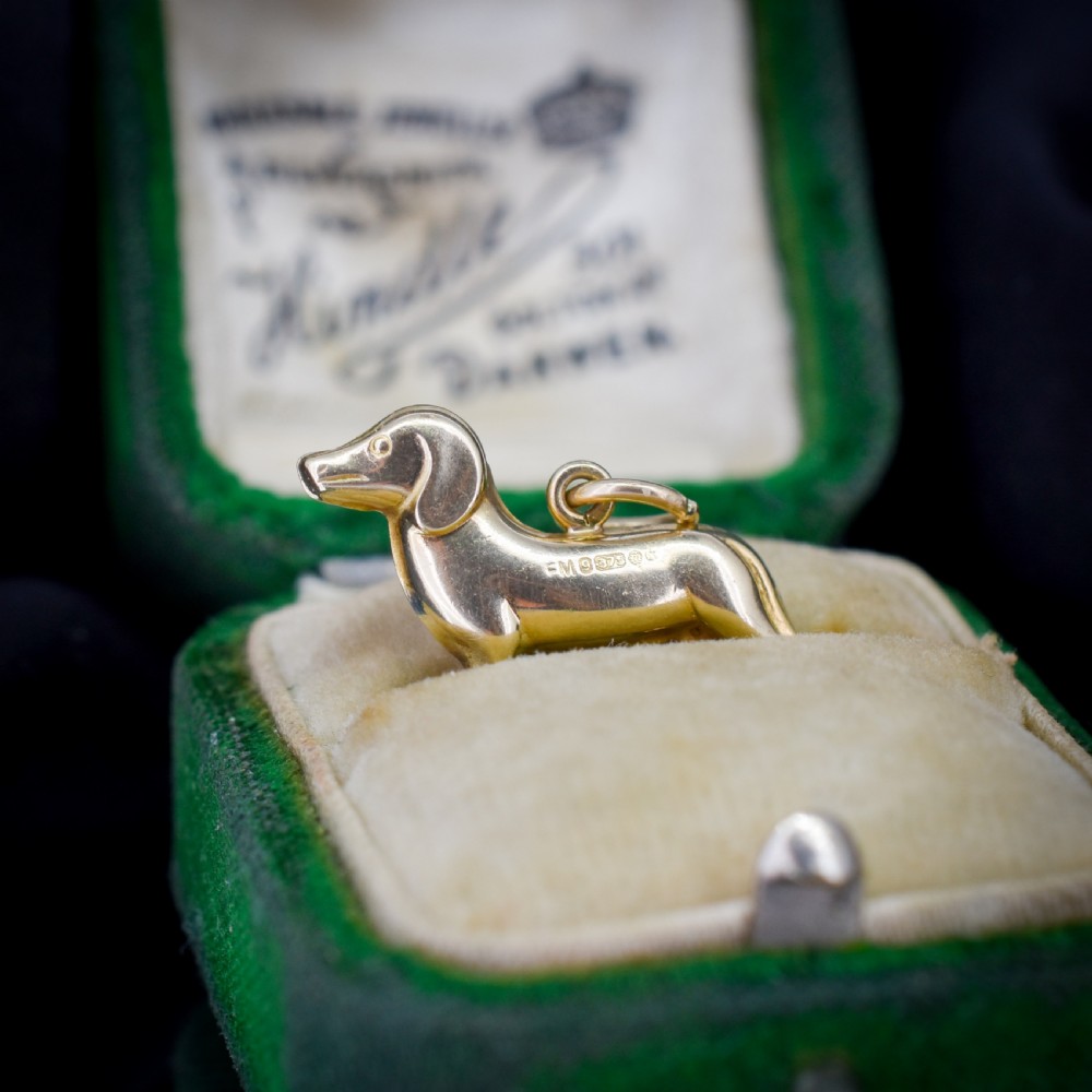 A solid 9ct yellow gold dachshund dog charm featuring detailed eye engravings and visible hallmarks along its body. View IV