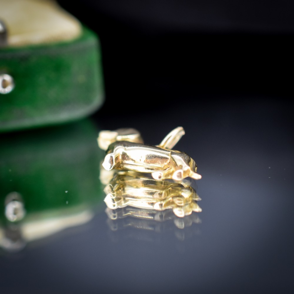 A solid 9ct yellow gold dachshund dog charm featuring detailed eye engravings and visible hallmarks along its body. View V