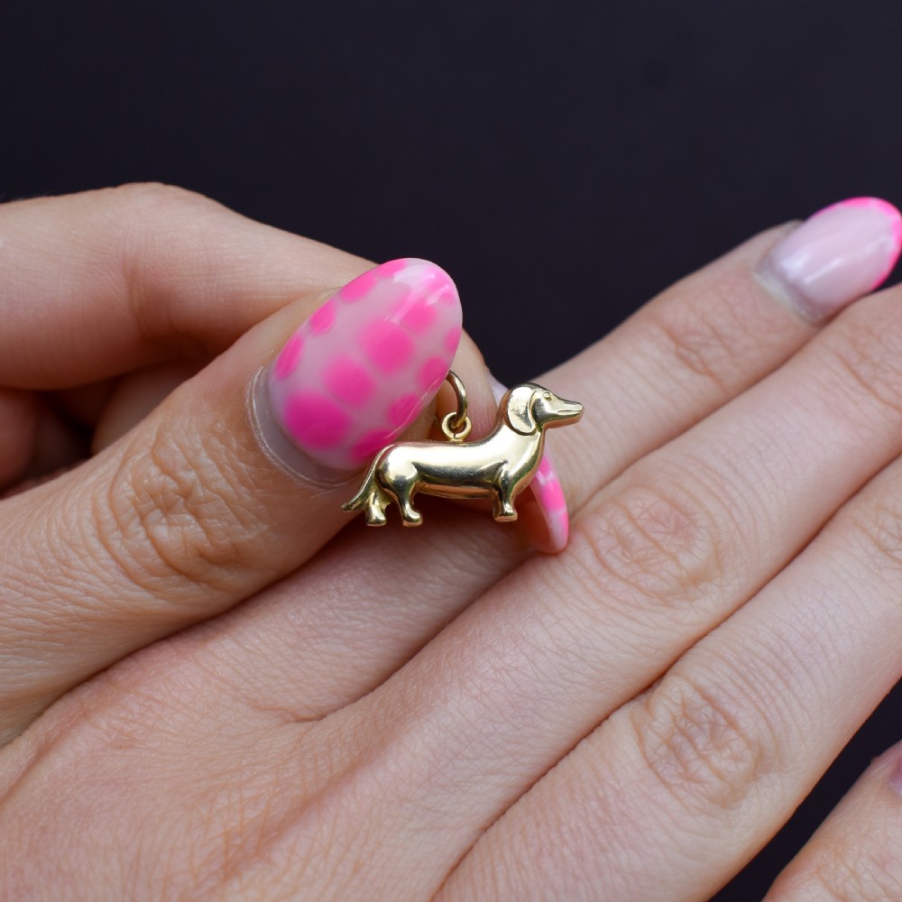 A solid 9ct yellow gold dachshund dog charm featuring detailed eye engravings and visible hallmarks along its body. View VI
