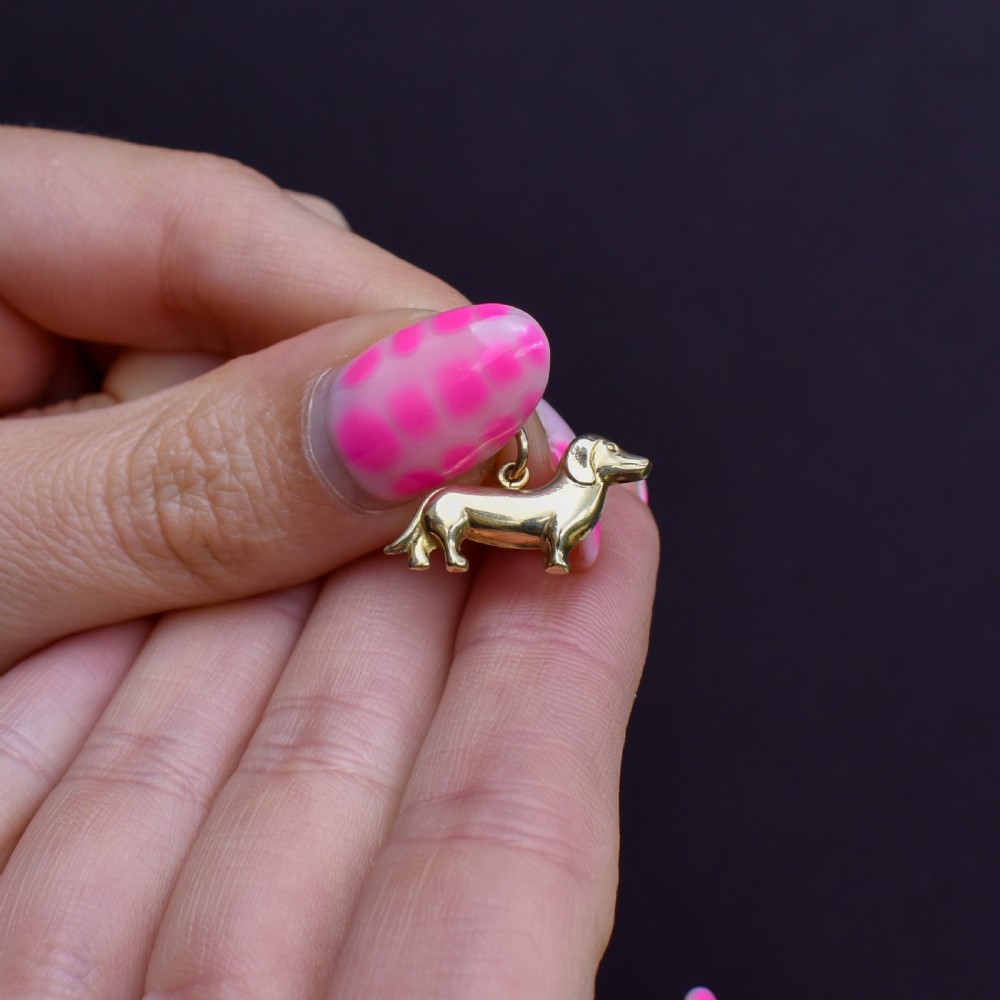 A solid 9ct yellow gold dachshund dog charm featuring detailed eye engravings and visible hallmarks along its body. View VII