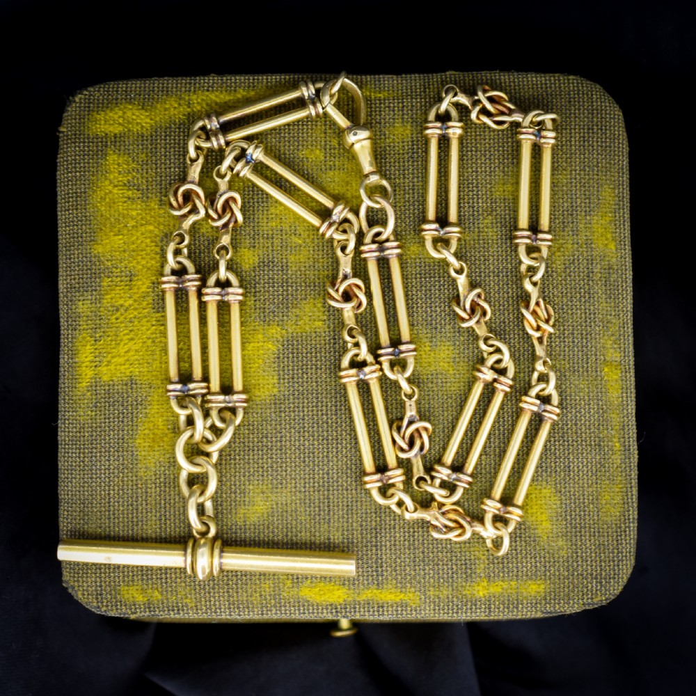 An antique 18ct yellow gold Albert chain necklace displaying alternating trombone links and twisted love knots with a T-bar attachment.