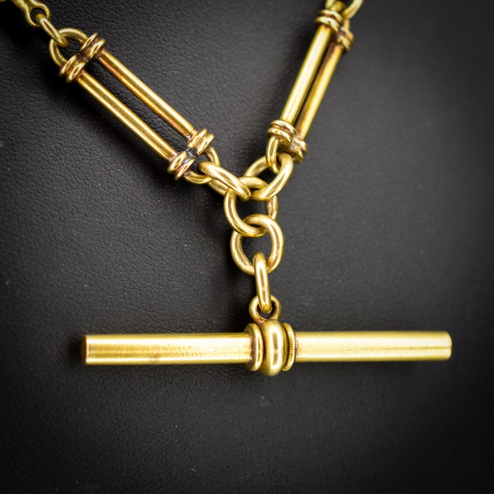 An antique 18ct yellow gold Albert chain necklace displaying alternating trombone links and twisted love knots with a T-bar attachment. View VI