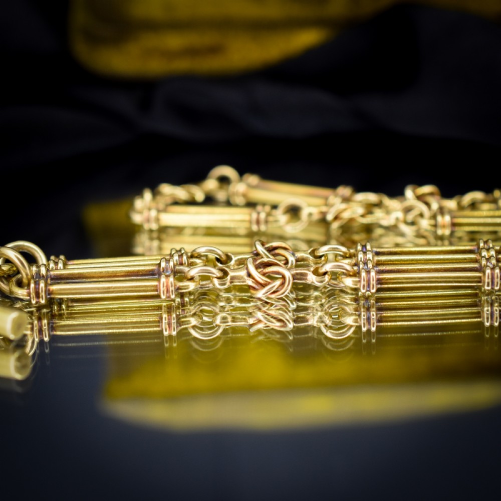An antique 18ct yellow gold Albert chain necklace displaying alternating trombone links and twisted love knots with a T-bar attachment. View IX