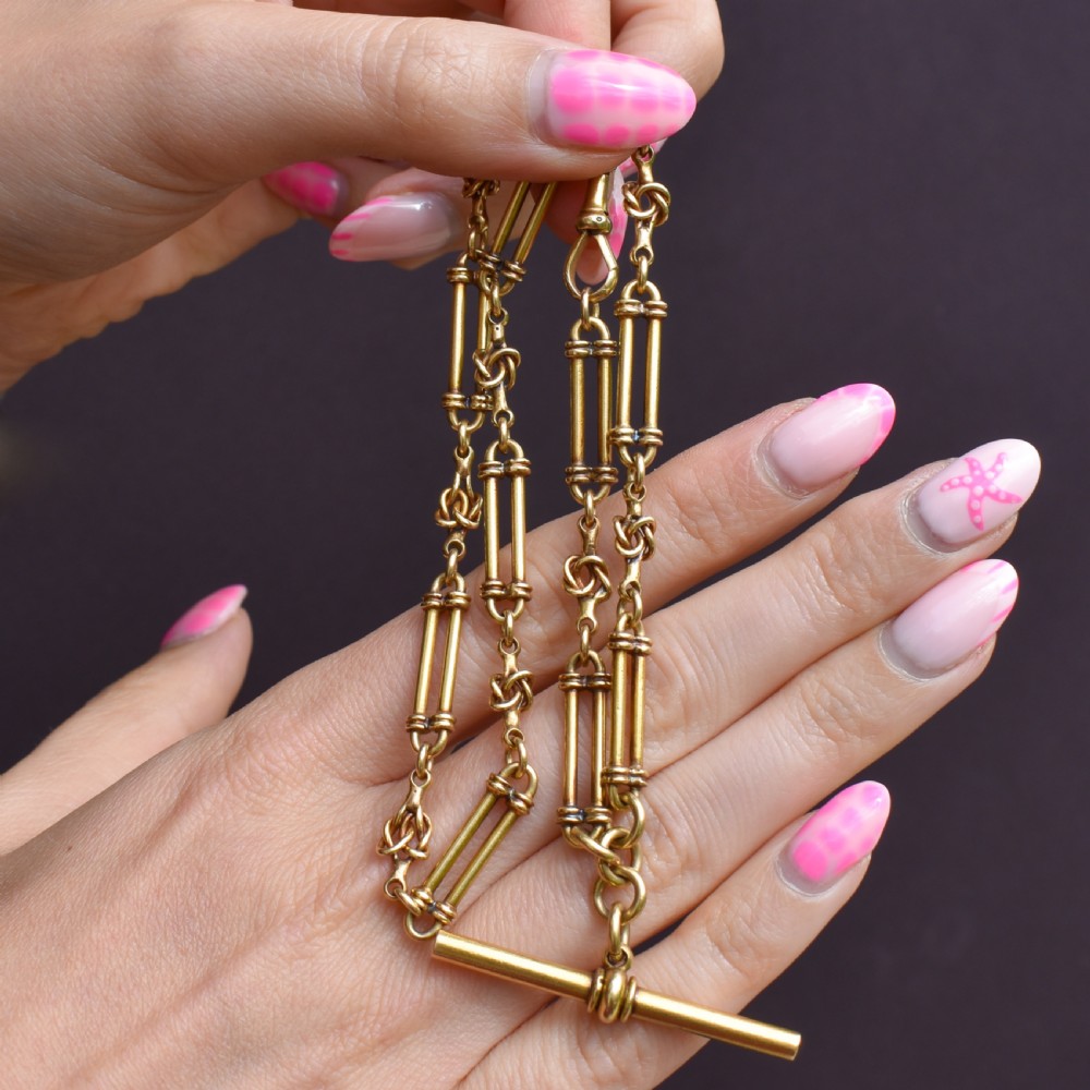 An antique 18ct yellow gold Albert chain necklace displaying alternating trombone links and twisted love knots with a T-bar attachment. View X
