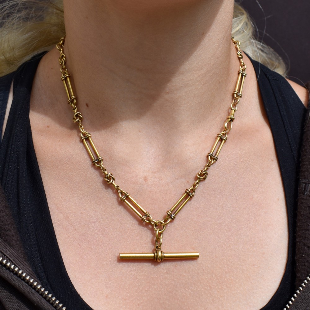 An antique 18ct yellow gold Albert chain necklace displaying alternating trombone links and twisted love knots with a T-bar attachment. View XI