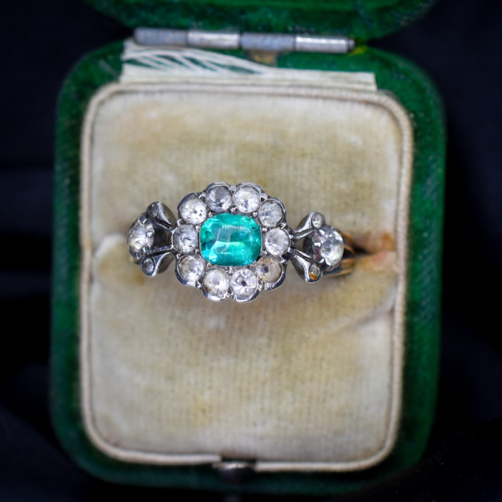 An antique Georgian cluster ring featuring a central cushion-cut green paste stone surrounded by clear paste stones set in silver and gold.