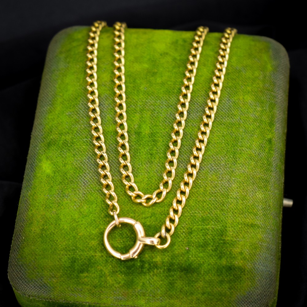 An antique 18ct yellow gold curb link chain necklace featuring a circular bolt ring clasp on a green velvet surface.