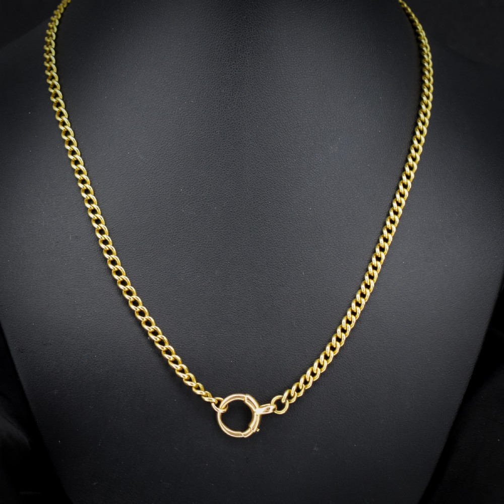 An antique 18ct yellow gold curb link chain necklace featuring a circular bolt ring clasp on a green velvet surface. View II