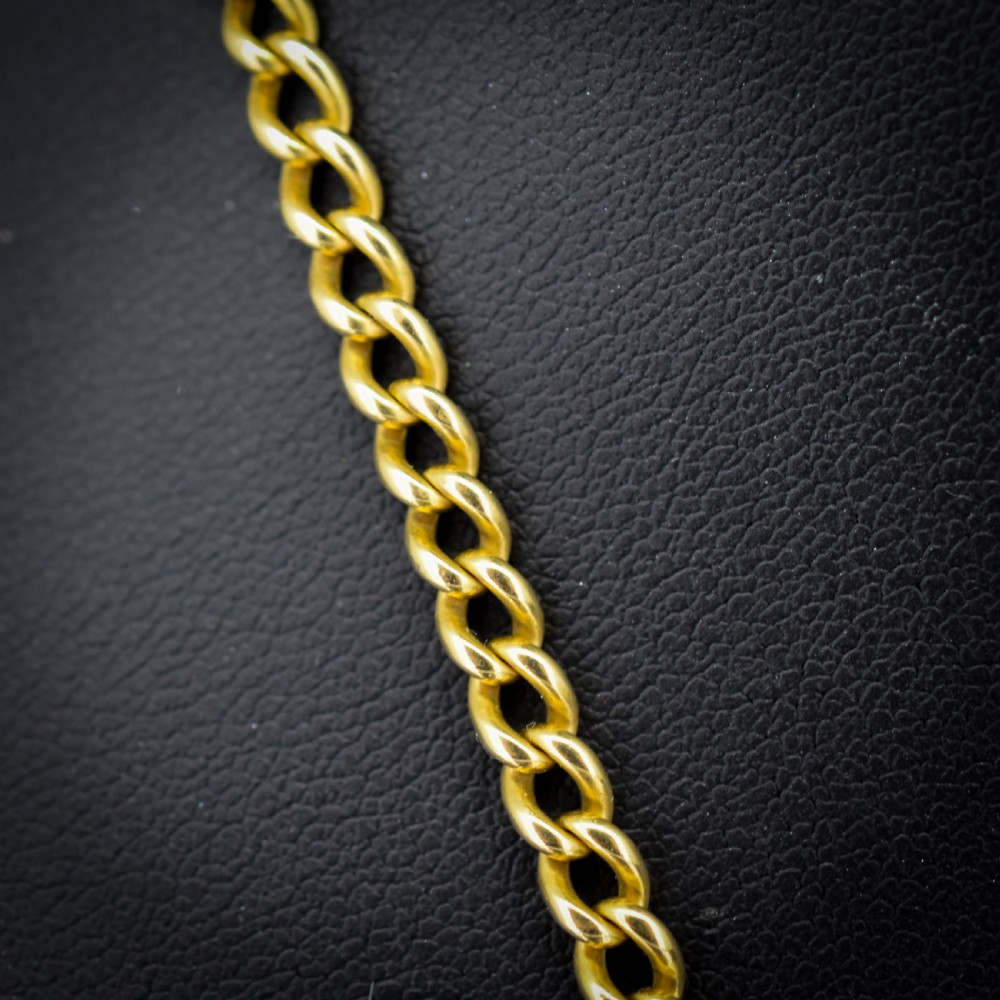 An antique 18ct yellow gold curb link chain necklace featuring a circular bolt ring clasp on a green velvet surface. View III